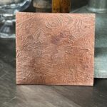 Engraved square metal plate with abstract designs.