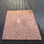 Etched copper plate on dark wooden surface.