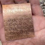 Hand holding patterned copper sheet rectangle.