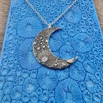 Silver crescent moon necklace on blue background.