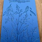 Blue botanical embossing mat on wooden surface.