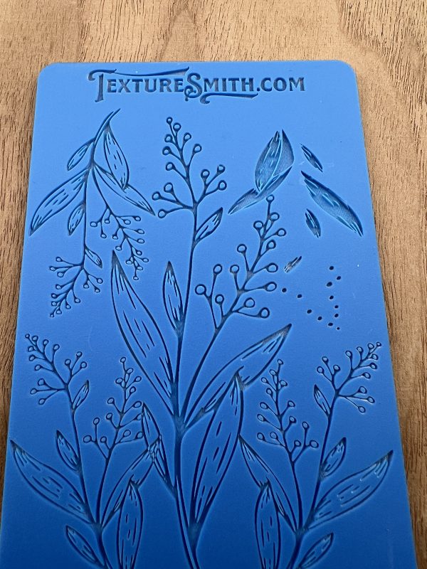 Blue botanical embossing mat on wooden surface.