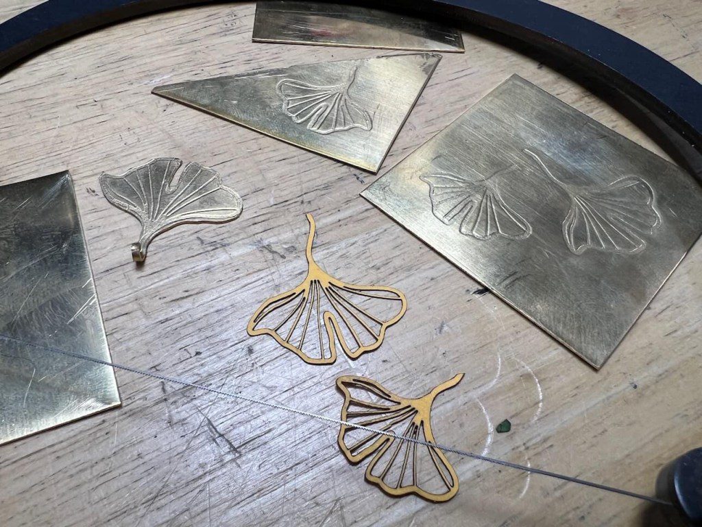 Metal ginkgo leaf designs and wire earrings on a wooden surface.