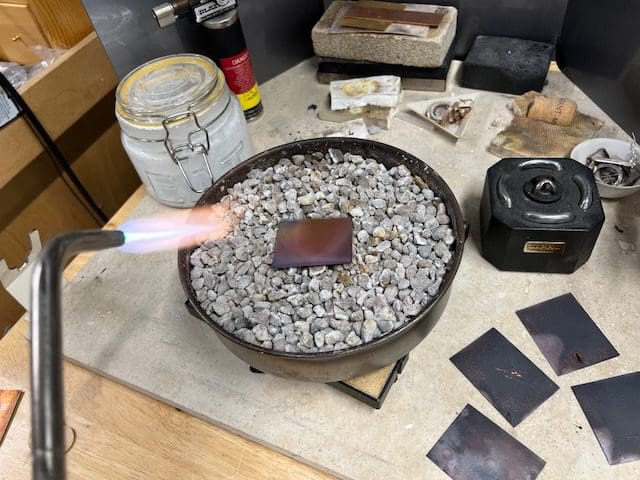 Person using a torch to heat a metal piece on a bed of stones.