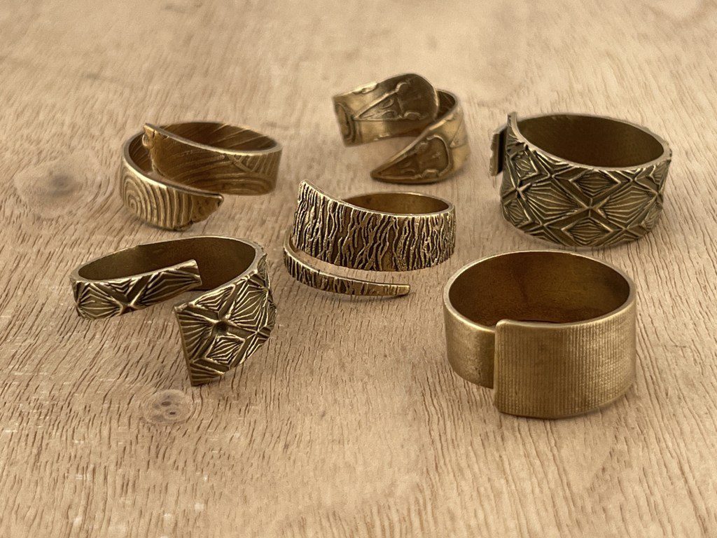 A collection of seven rustic metal rings on a wooden surface.