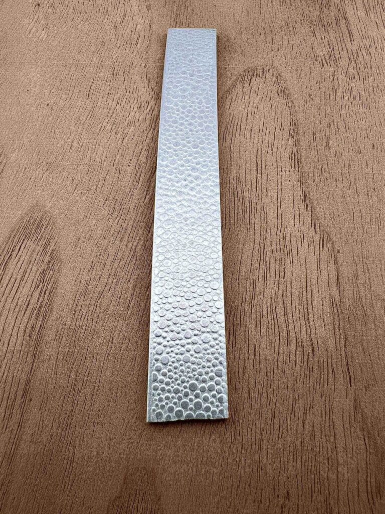 A textured metallic strip on a wooden surface.
