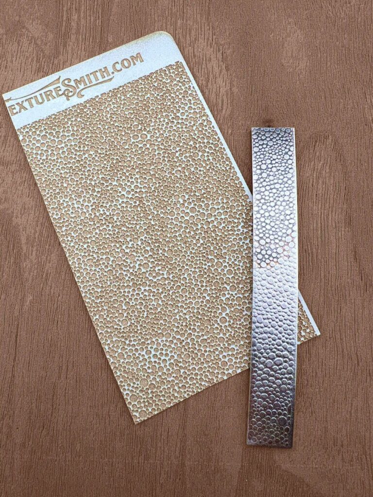 Two sheets of textured silver adhesive foil on a wooden surface.