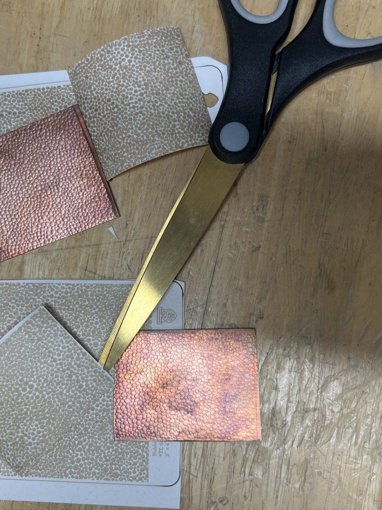 A pair of scissors cutting pink fabric on a wooden surface.