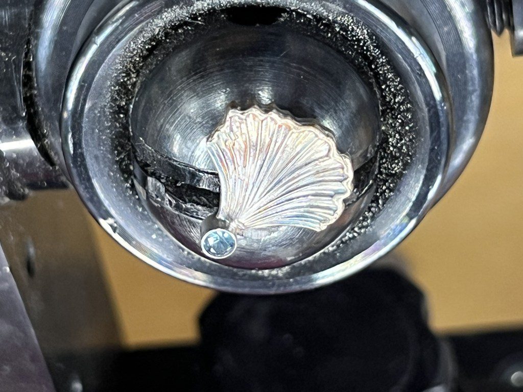 A seashell-shaped metal detail inside a circular silver object.
