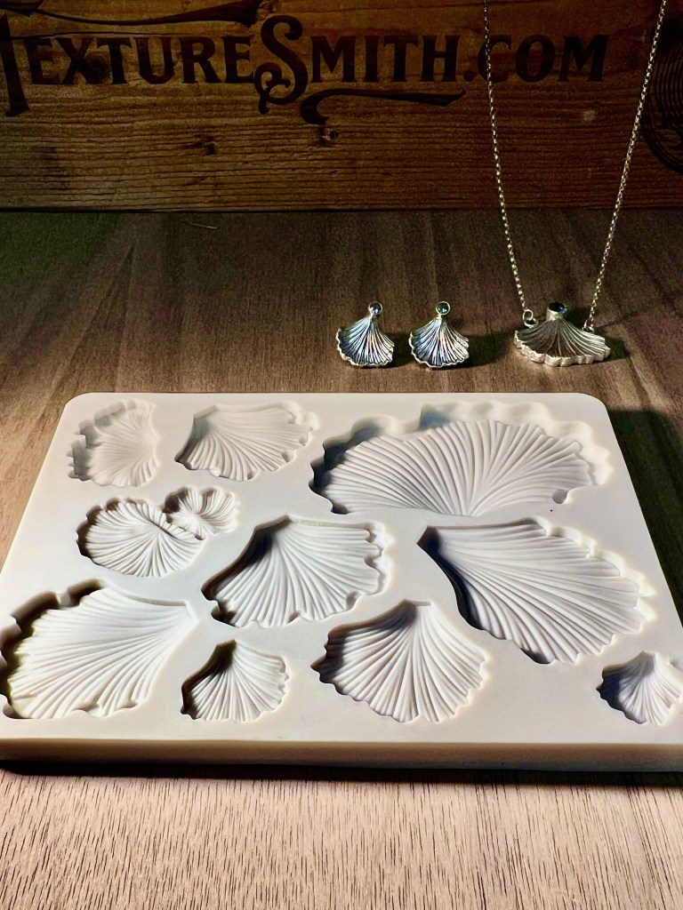 White ceramic seashell molds on a wooden table with hanging shells above.