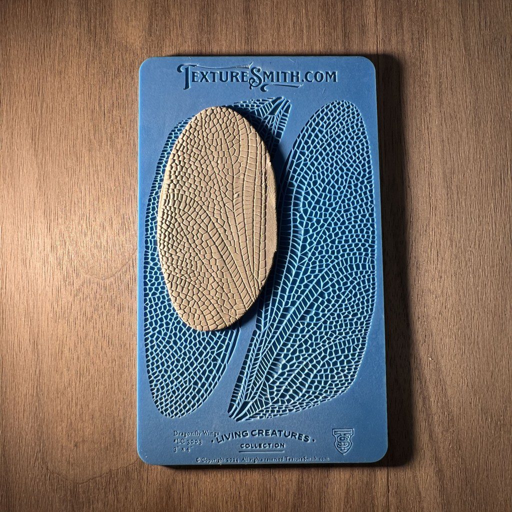 Blue textured art piece with oval burlap centerpiece on wooden surface.