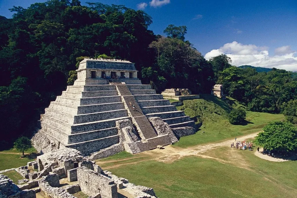 Ancient stepped pyramid under a blue sky surrounded by greenery.