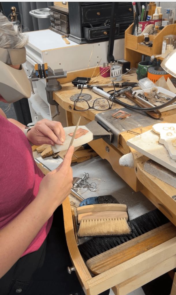 Person working on detailed jewelry crafting at a cluttered workstation.