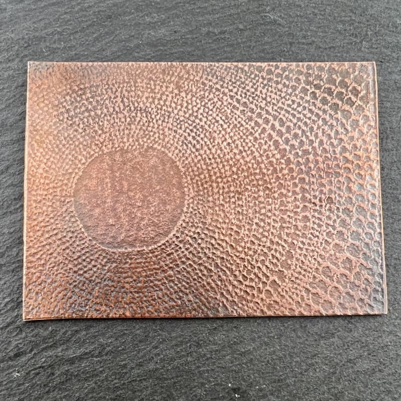 A textured rectangular copper plate with an embossed circular design.