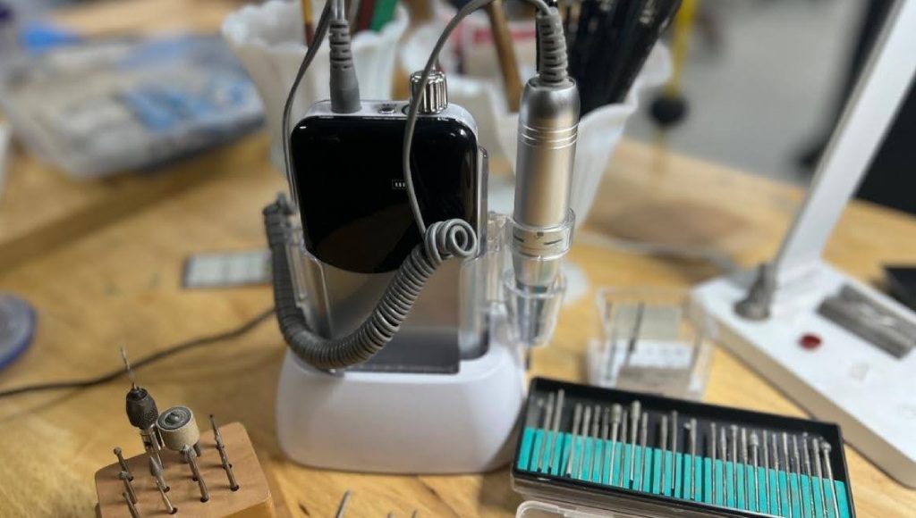 Portable dental scaler with tips and smartphone holder on white base.