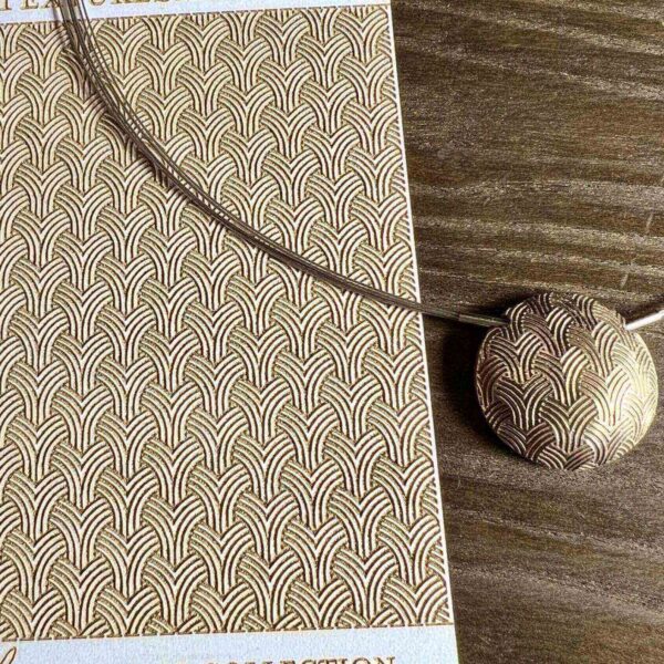 A textured notebook with a cord and round pendant on a wooden surface.