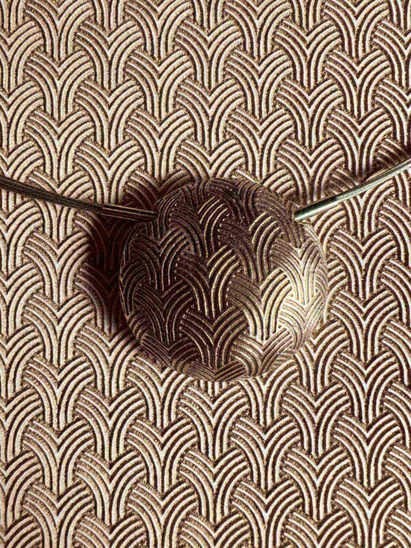 An artistic metal ladle with a patterned background.