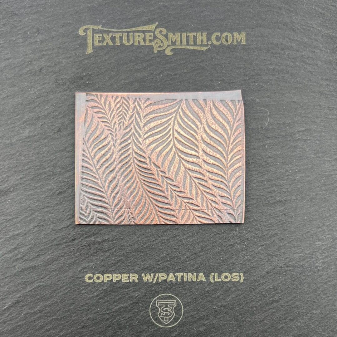 Copper-colored square with wavy leaf-like patterns on a dark background.