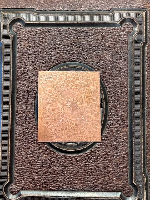 A small square artwork with abstract patterns on a textured brown background.