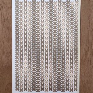 A sheet of paper with a repetitive floral pattern placed on a wooden surface.