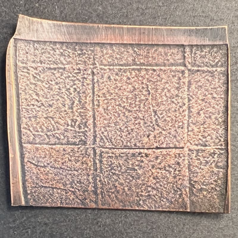 Square copper art piece with abstract textured patterns.