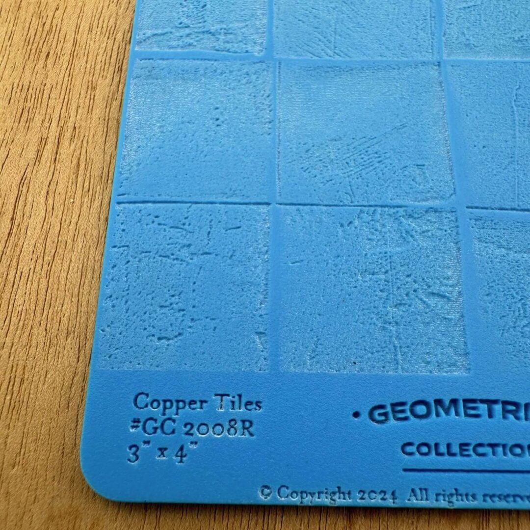 Close-up of a blue copper tile sample with text on a wooden surface.
