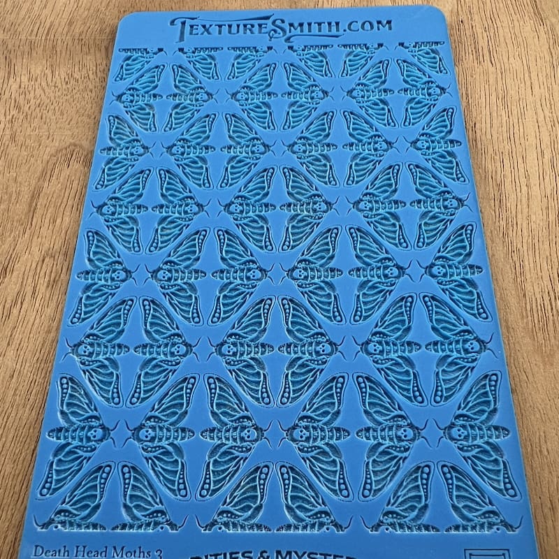 Blue stencil sheet with intricate patterns on a wooden surface.