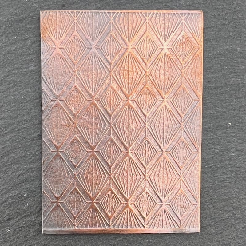 A small, textured rectangular object with a diamond pattern on a dark surface.