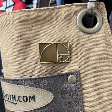 Close-up of a beige bag with a geometric pin and a partial logo patch.