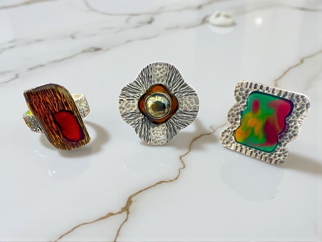 Three colorful, handcrafted rings displayed on a marble surface.