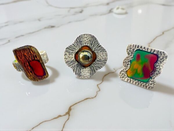 Three unique, colorful rings displayed on a white marble surface.