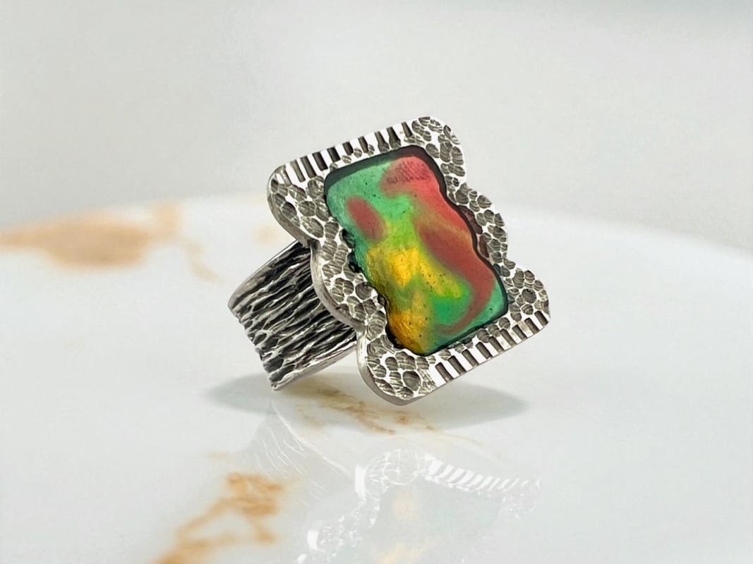 Intricately designed silver ring with a vibrant, multicolored gemstone.