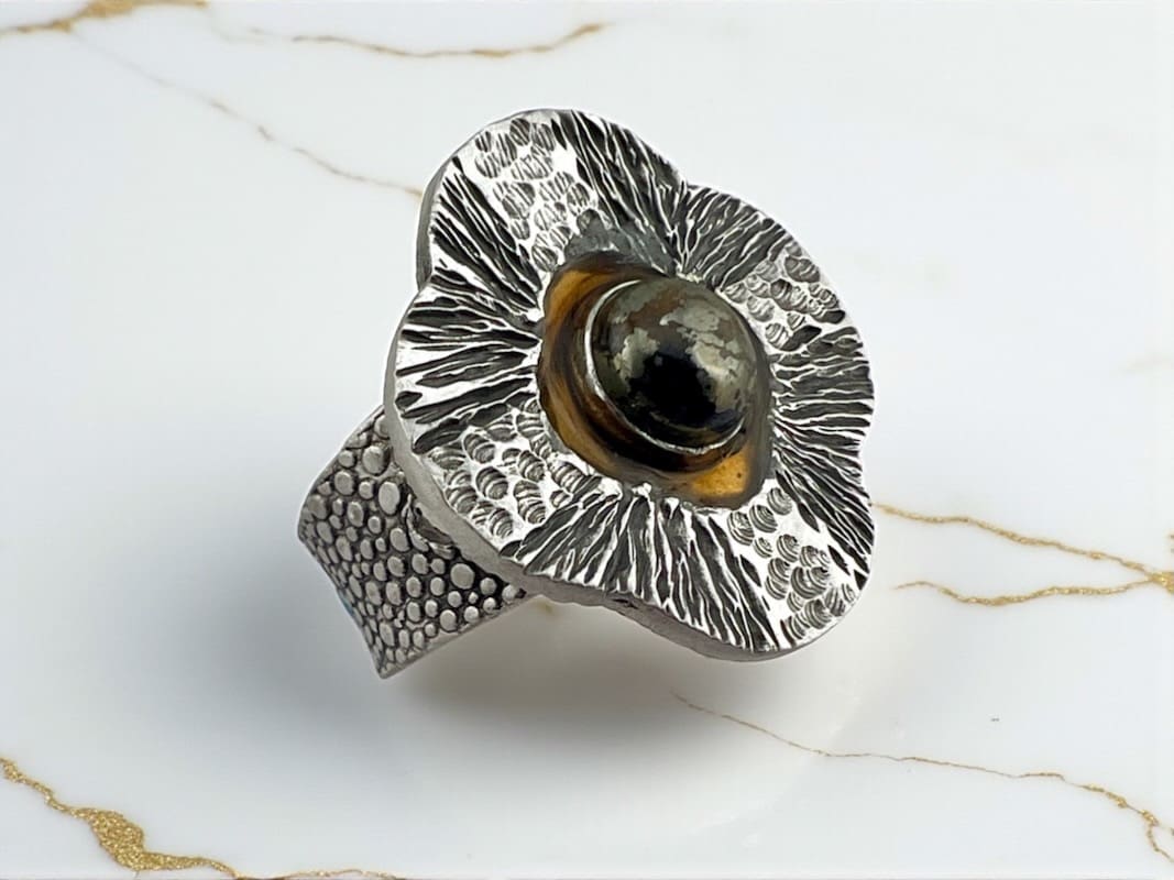 Close-up of a silver flower-shaped ring with a dark stone center.