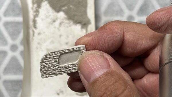 Hand holding a small, textured rectangular object with a cut-out.