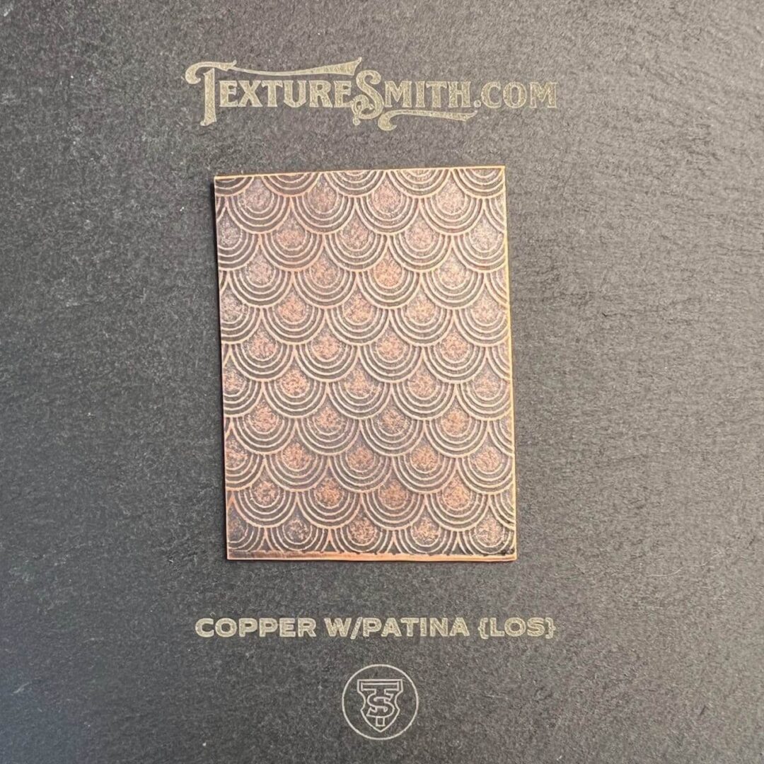 Copper w/patina metal sheet with intricate pattern on gray background.