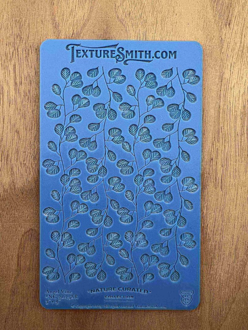 Blue stencil sheet with small ginkgo leaf cutouts on wooden surface.