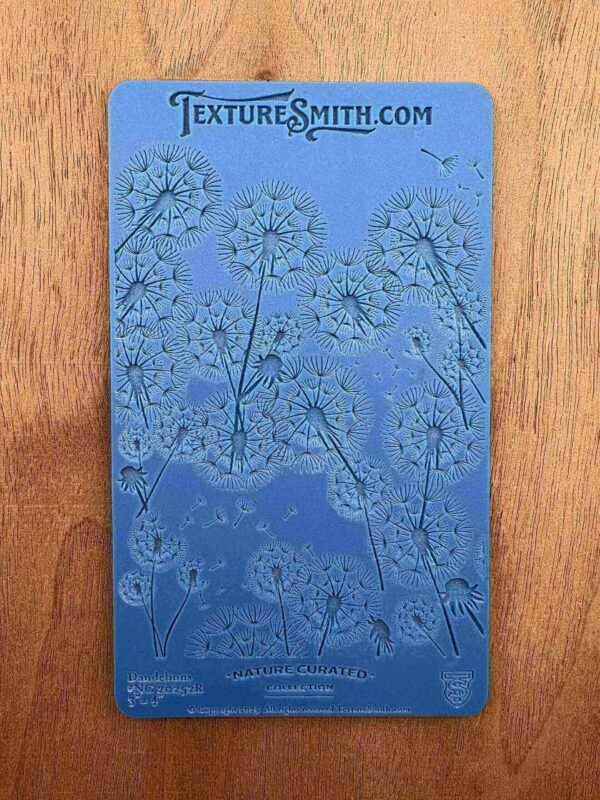 Blue embossing stencil with floral and swirl patterns on wood.