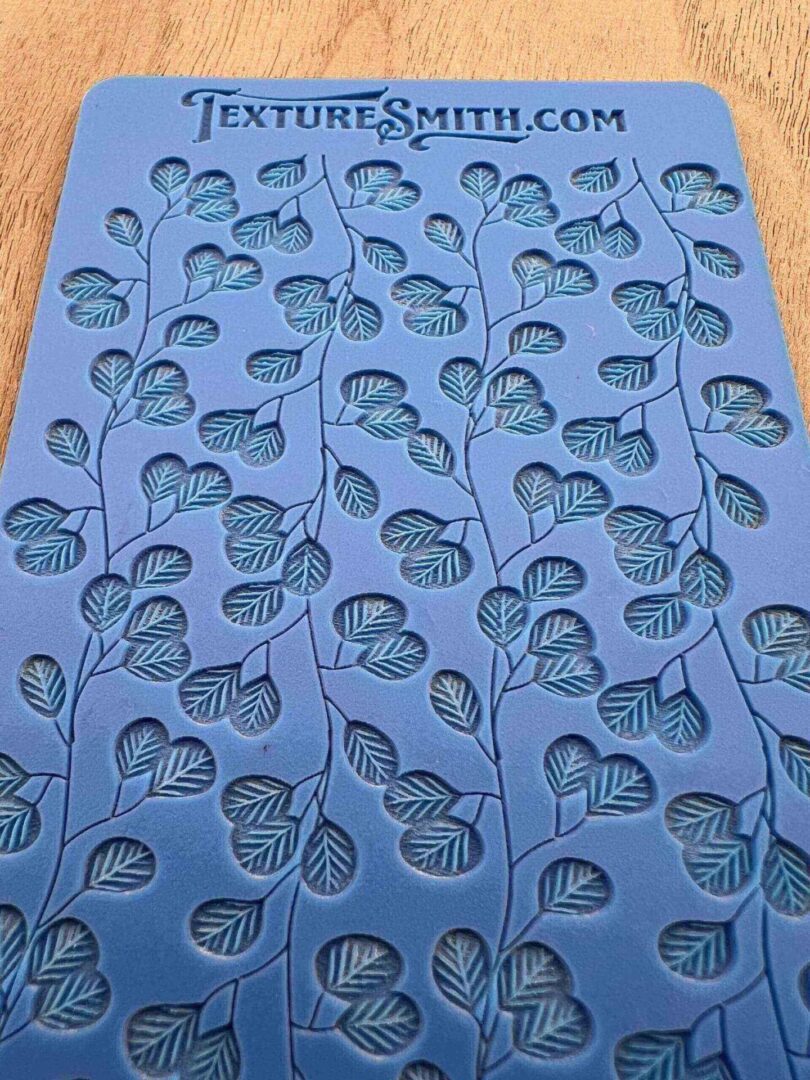 Blue fabric with a repeating pattern of black leaves and hearts.