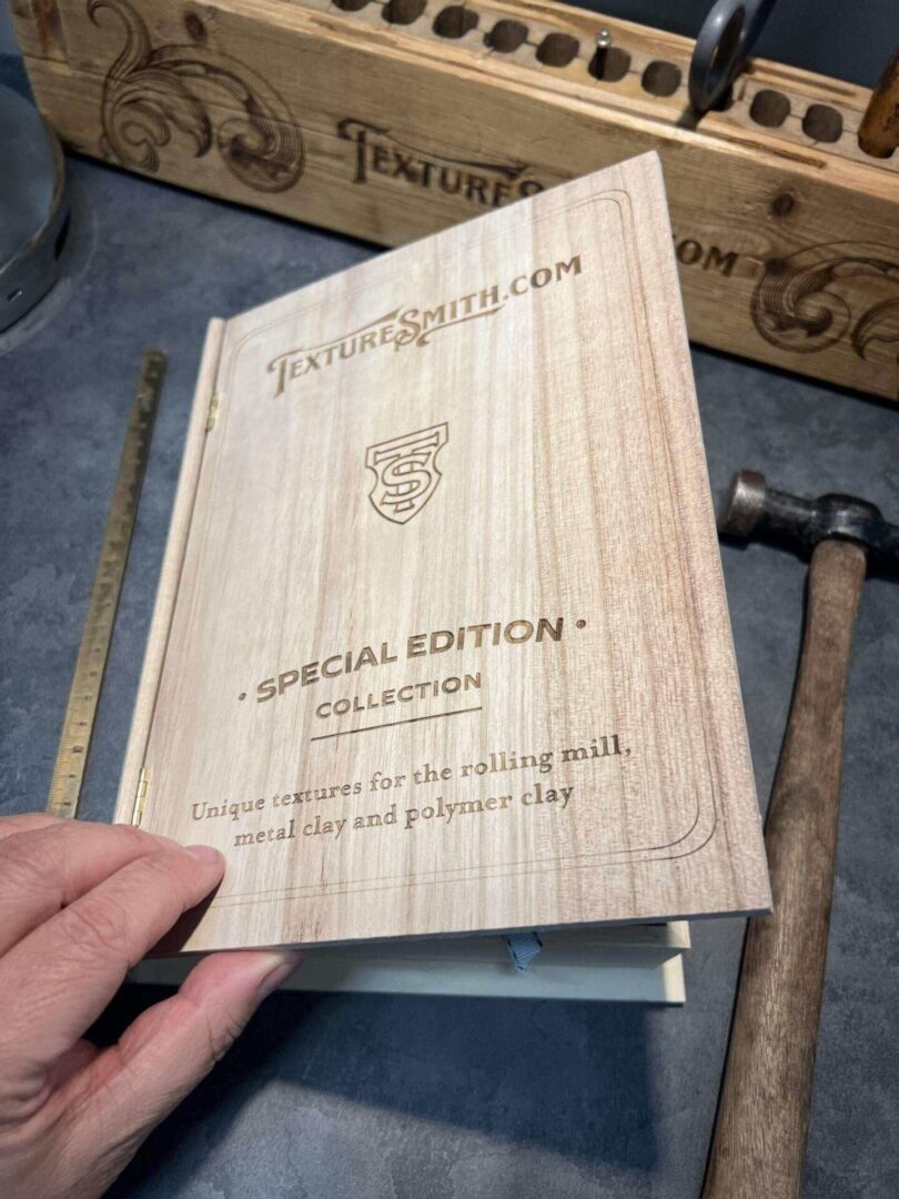 A hand holding a wooden cover book titled 'The Treasure Chest' with a hammer in the background.
