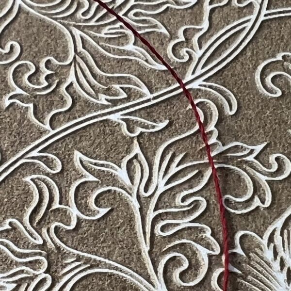 Close-up of intricate embroidery with white and red threads on textured fabric.