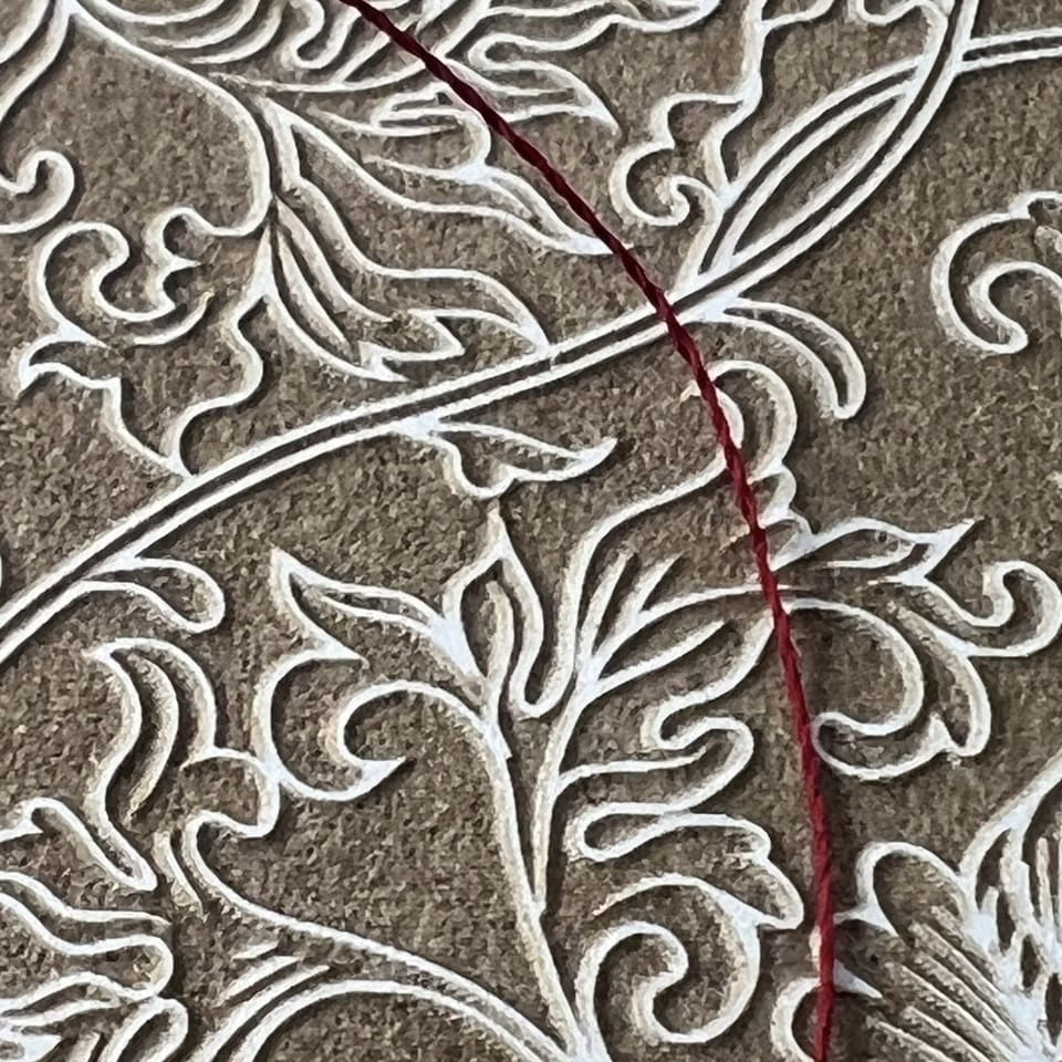 Close-up of intricate embroidery with white and red threads on textured fabric.