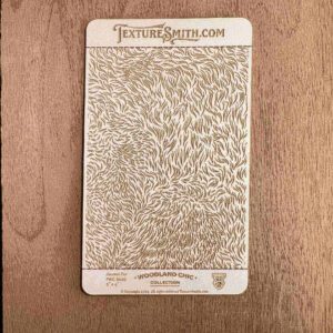 Intricate gold floral design on a card against a wooden background.
