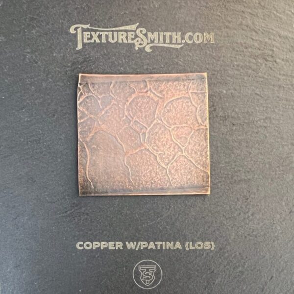 Square copper tile with intricate floral pattern on a dark background.