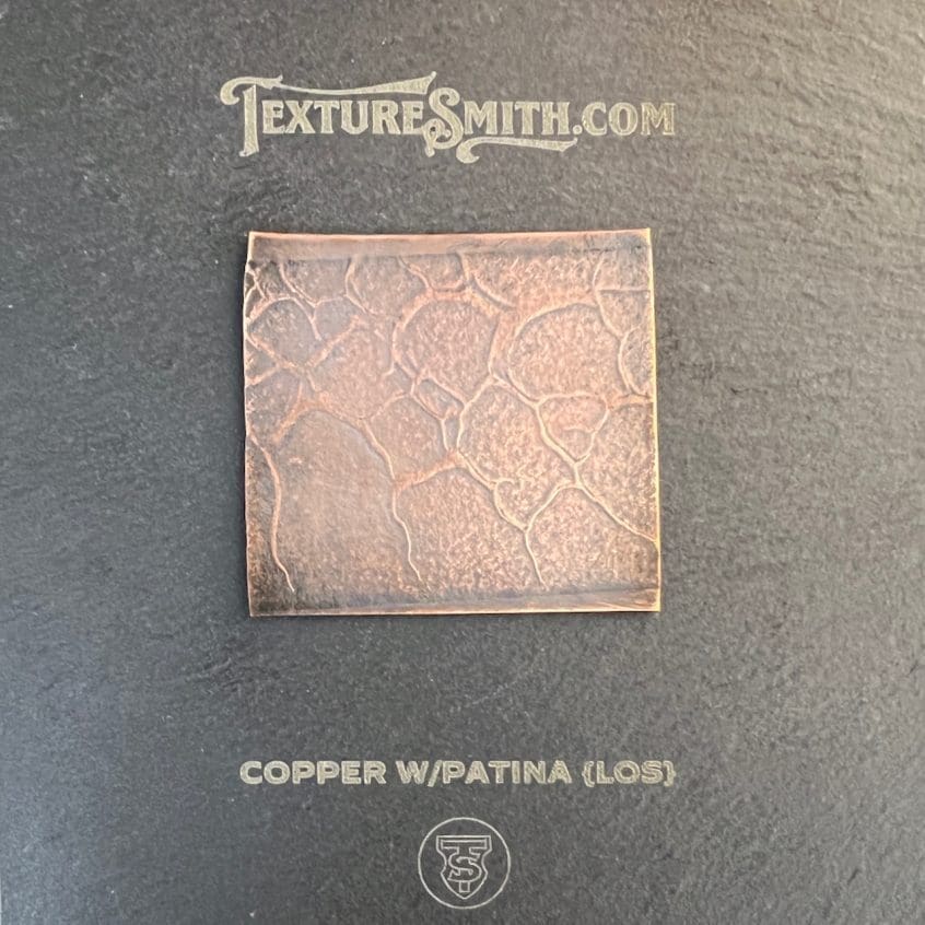 Square copper tile with intricate floral pattern on a dark background.