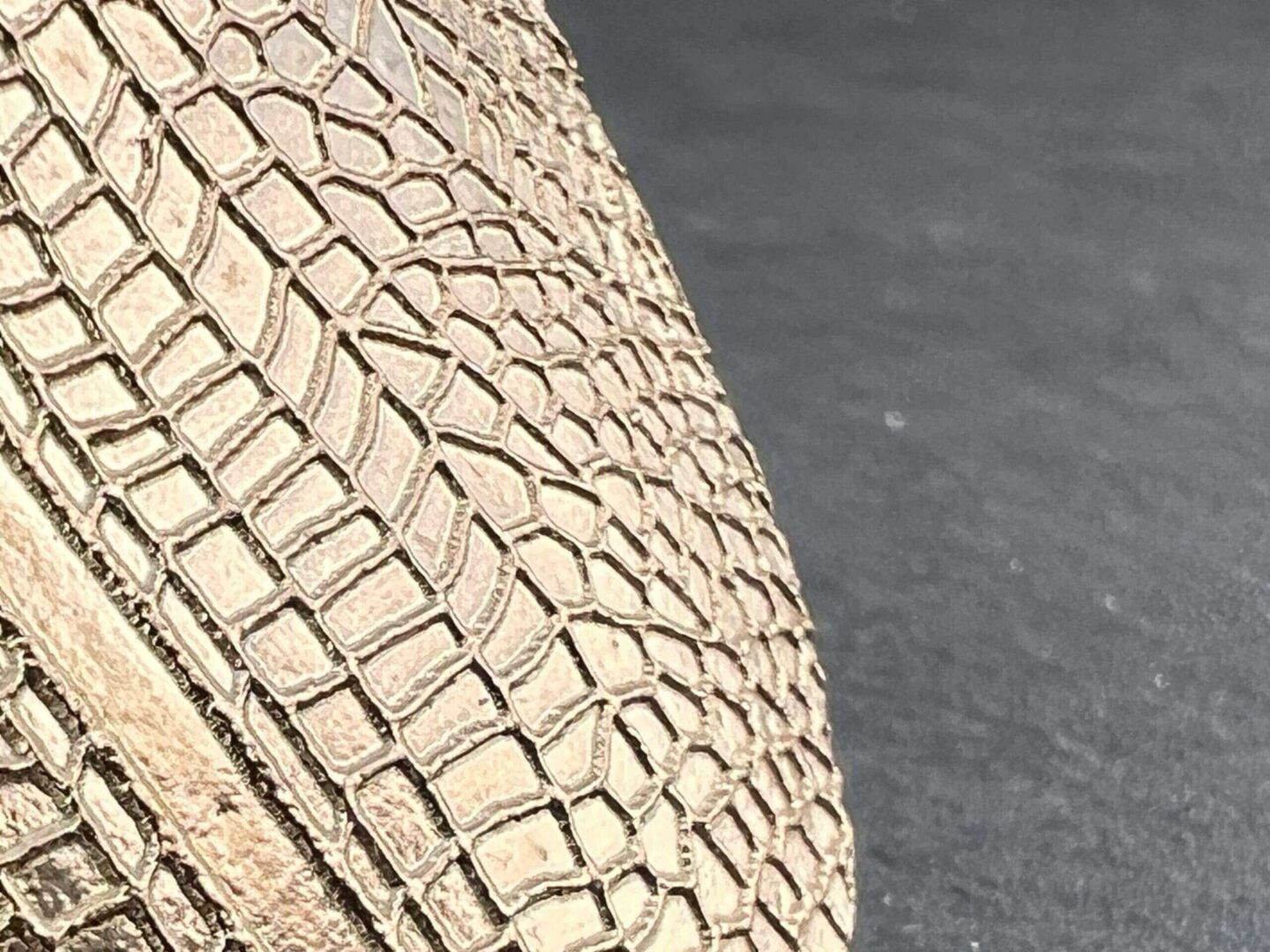 Close-up of a textured beige woven handbag on a gray surface.