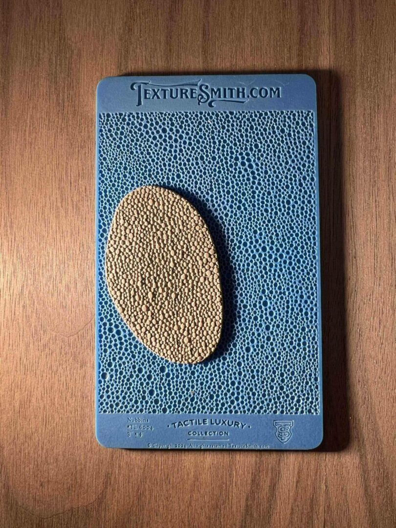 A textured blue card with an oval beige stone attached.
