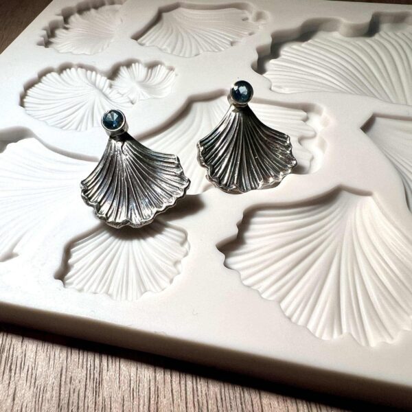 Elegant silver fan-shaped earrings on a textured surface.