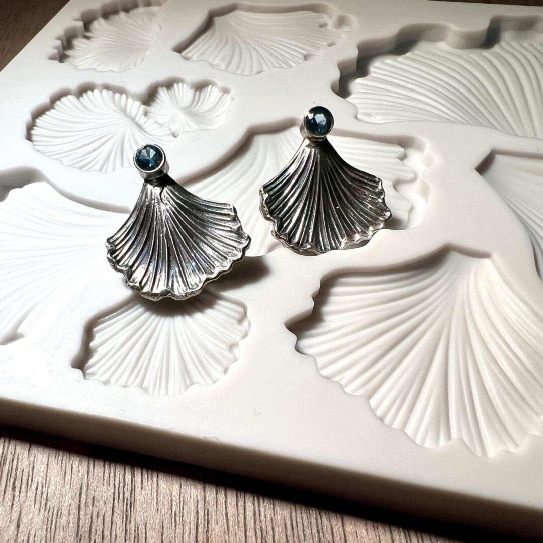 Elegant silver fan-shaped earrings on a textured surface.