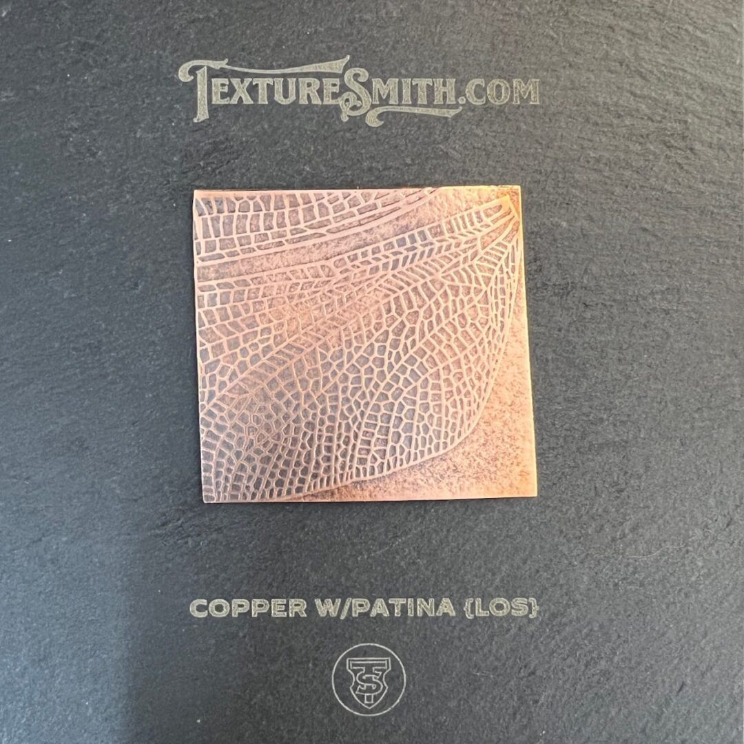 A square copper sheet with a textured pattern on a dark background.