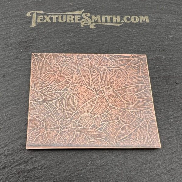 A textured copper sheet with intricate patterns on a dark background.